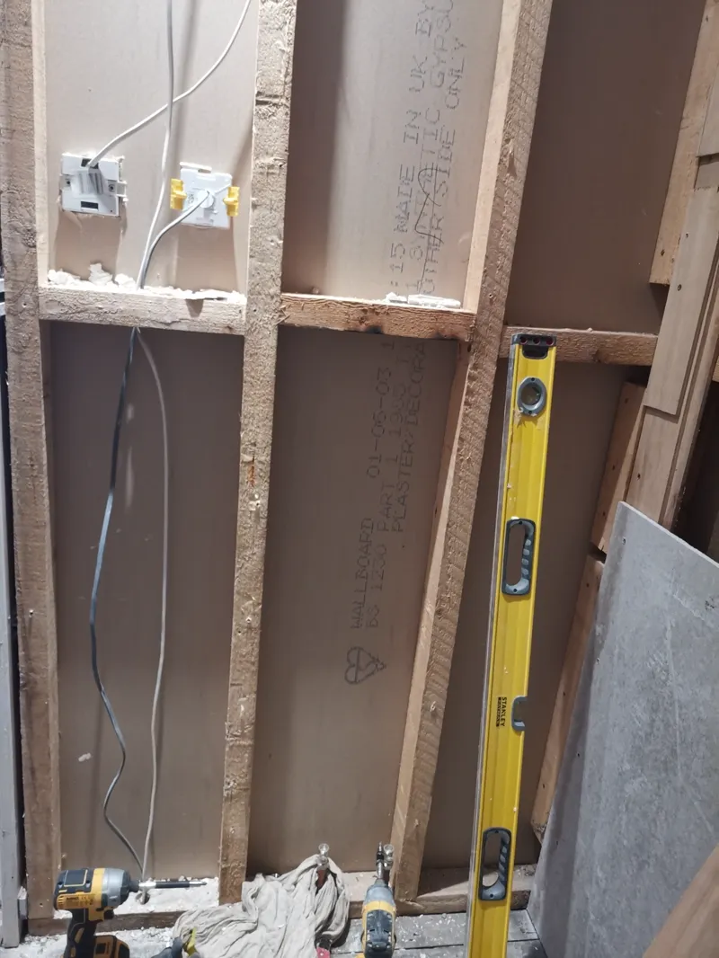 Timber stud wall with a first-fix electrical socket box and cabling, spirit level against the frame.