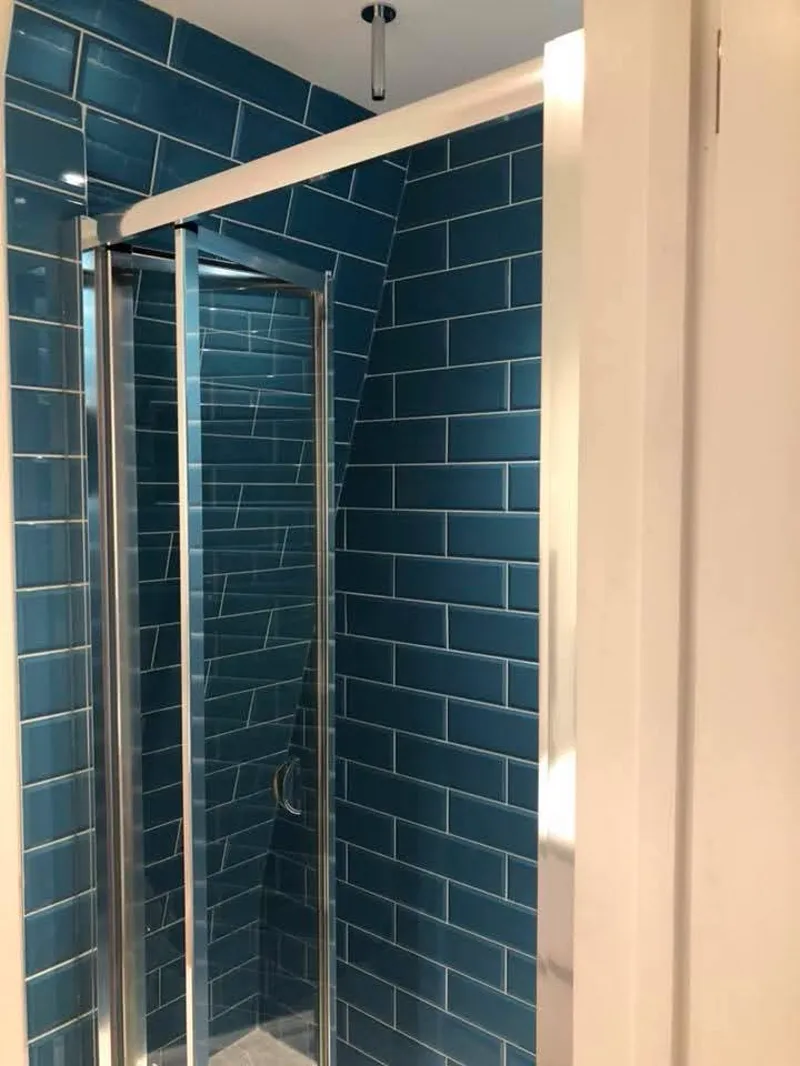 Completed shower enclosure with dark teal metro tiles and a glass sliding door.