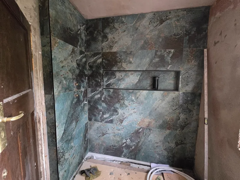 Completed shower enclosure in dark stone-effect tiles with a recessed shelf niche.