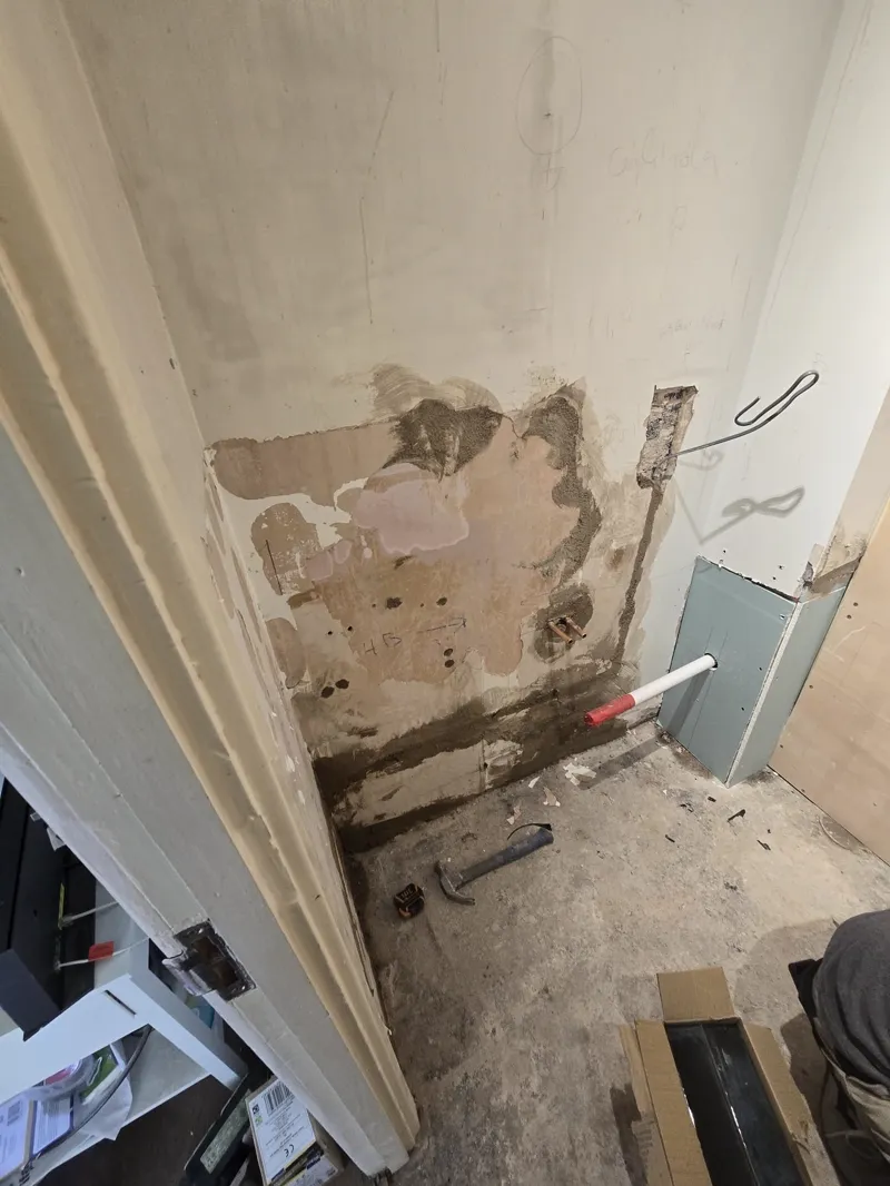 Water-stained bathroom wall corner with a pipe fitting, ready for repair.
