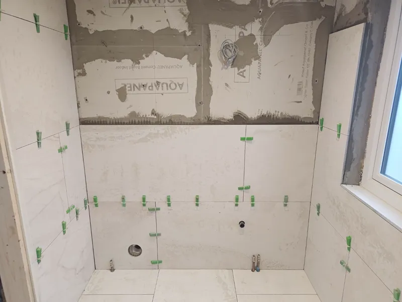 Tiled shower walls with spacers in place, cement backer board visible above, small window in the corner.