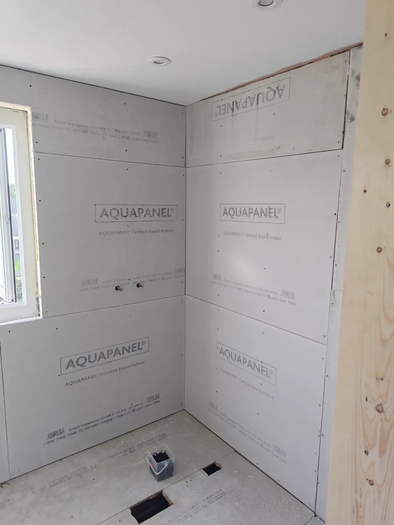 Cement backer board installed across bathroom walls, downlights fitted in the ceiling, ready for tiling.