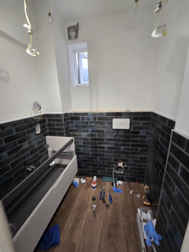 Near-complete bathroom with black metro-tiled walls, a white shower tray and wood-effect flooring.