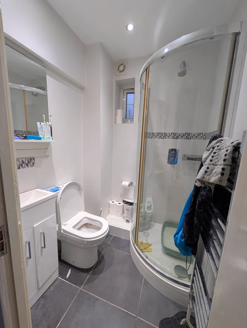 Completed bathroom with a curved glass shower enclosure, grey floor tiles and white sanitaryware, a garment hung on the heated towel rail.